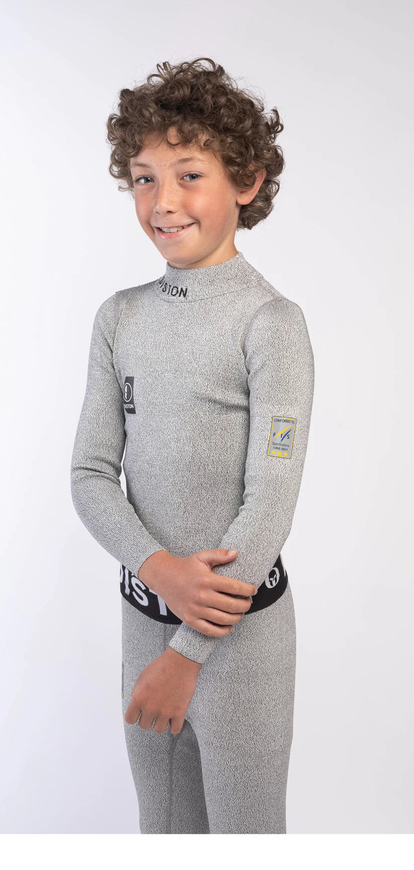 Ein Junge mit lockigem braunem Haar lächelt in die Kamera. Er trägt eine Diston DISTON Cut Resistant Unterhose Junior - 4FIS Stars in CRG - CORE / Racing Fit und steht vor einem schlichten weißen Hintergrund.