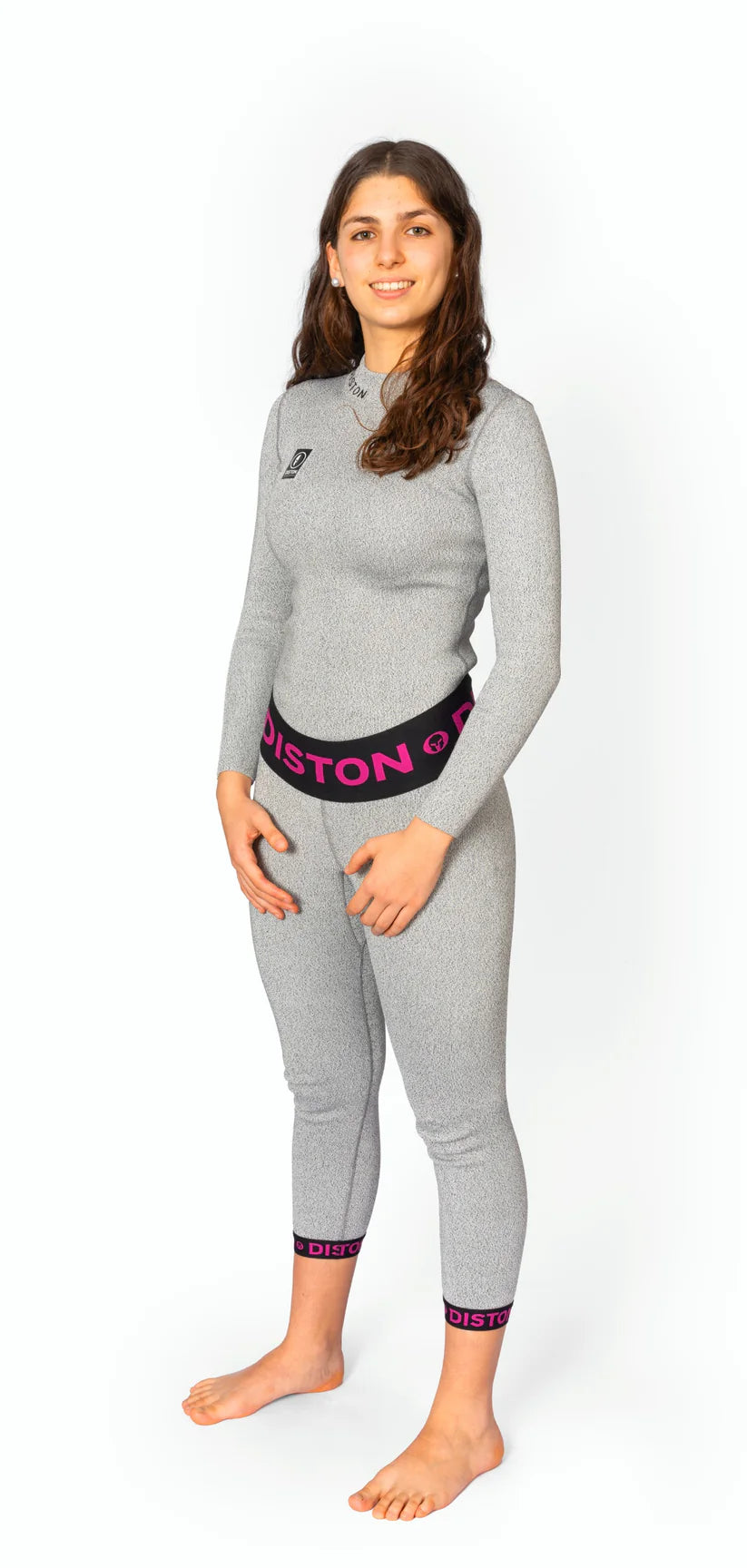 Eine junge Frau mit langen braunen Haaren steht barfuß, lächelt und trägt eine Diston DISTON WC Cut Resistant Unterhose Women-CORE / Racing Fit, mit "DISTON" in rosa auf Bund und Bündchen. Perfekt als Damen Ski Unterwäsche.