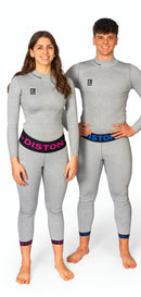 Ein Mann und eine Frau in passenden hellgrauen, taillierten Diston-Outfits mit rosa und blauen DISTON-Bünden lächeln vor einem weißen Hintergrund und präsentieren die DISTON WC Cut Resistant Unterhose Women - 4FIS Stars in CRG - CORE / Racing Fit.