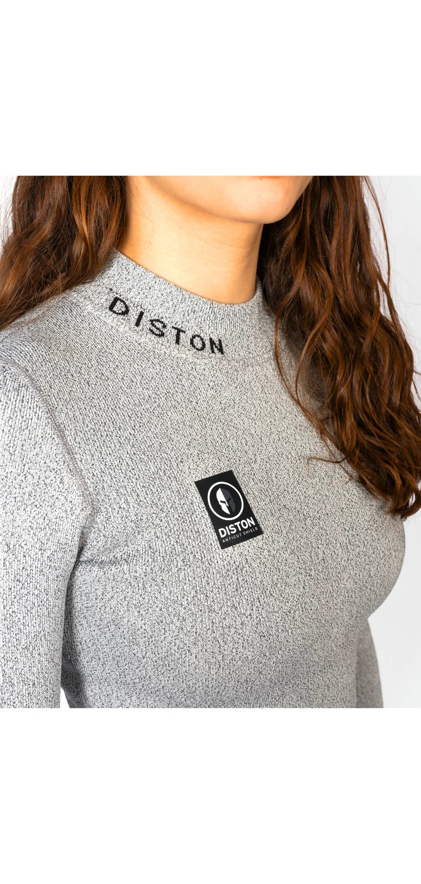 Eine Frau mit langen braunen Haaren trägt das Diston WC Cut Resistant Top Women - 4FIS Stars in CRG - CORE / Racing Fit mit grauem Rippenmuster, gesticktem "DISTON" in der Nähe des Kragens und einem schwarz-weißen rechteckigen Logoaufnäher auf der Brust.