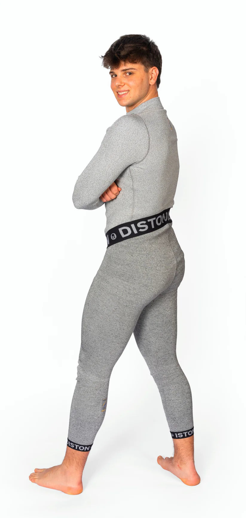 Ein junger Mann steht barfuß, zur Seite gedreht und über die Schulter blickend, in einer grauen Diston WC Cut Resistant Unterhose für Männer mit Racing Compression Fit und "DISTON"-Schriftzug an Bund und Bündchen vor weißem Hintergrund.