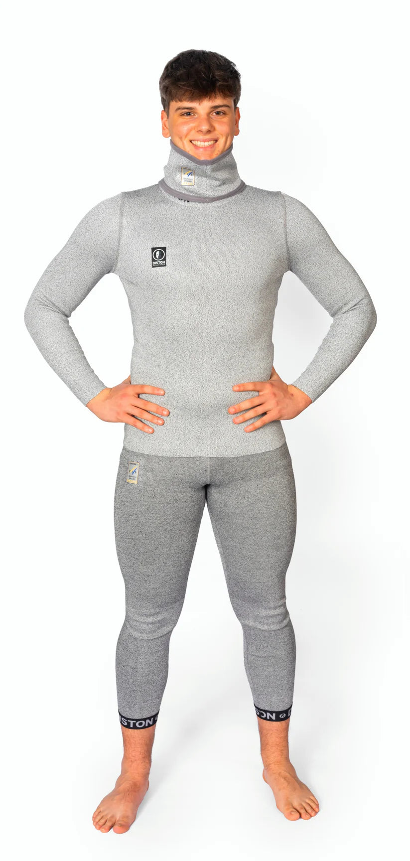 Ein Mann steht barfuß, lächelt und trägt Diston DISTON WC Cut Resistant Unterhosen Men - 5FIS Stars in CRG mit PRO/Racing Compression Fit. Er steht vor einem weißen Hintergrund, die Hände in die Hüften gestemmt.