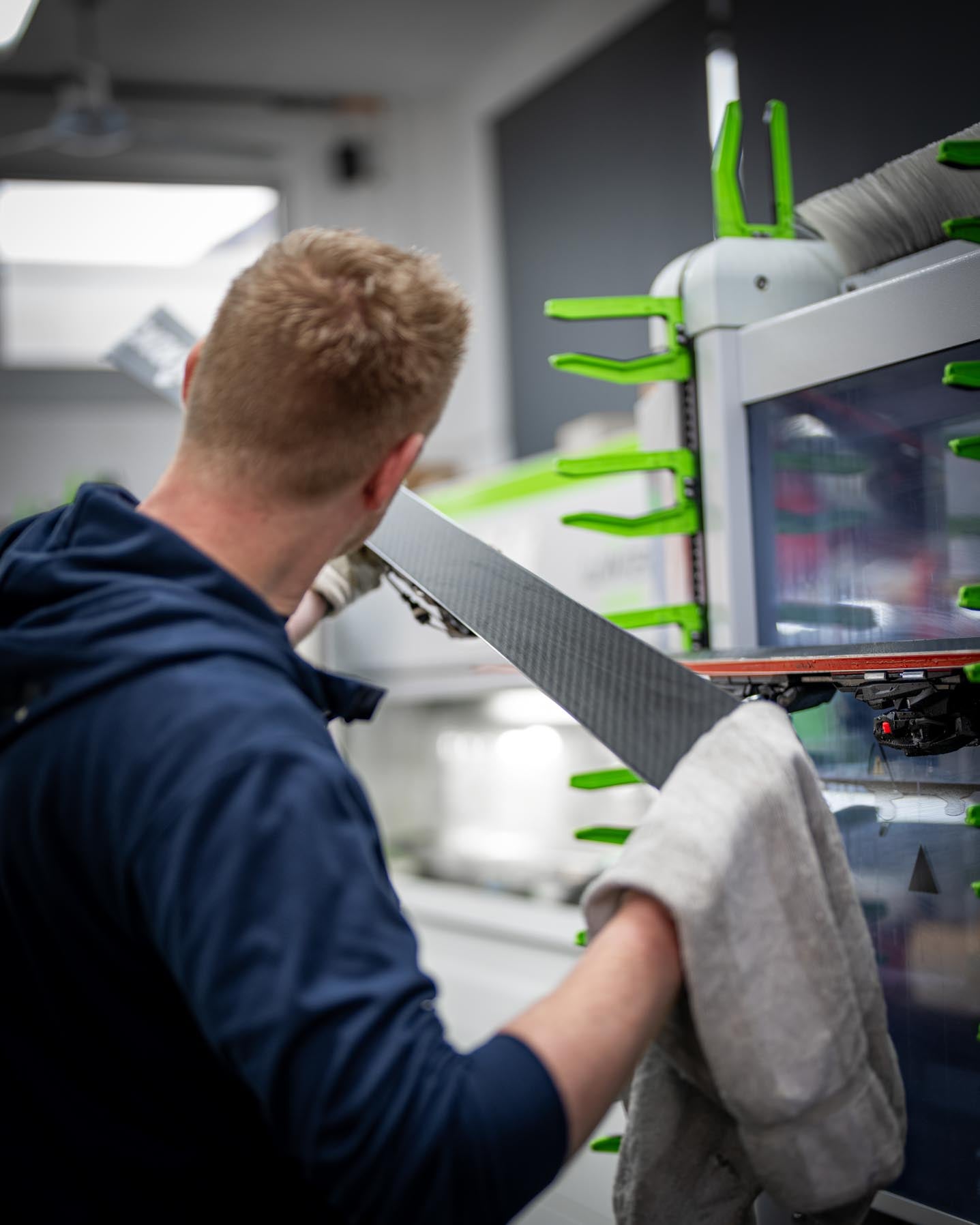 Eine Person überprüft die Struktur eines Snowboards, um sicherzustellen, dass der Belag optimal vorbereitet ist. Der Service umfasst präzise Bearbeitung und Qualitätskontrolle.