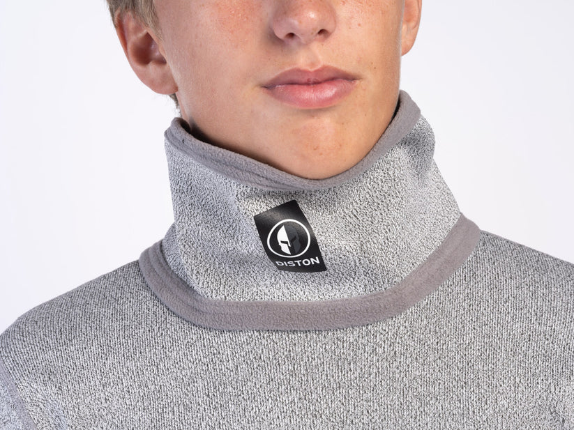 Eine Person trägt einen hellgrauen DISTON Cut Resistant Neck Guard - 4 FIS Stars in CRG (CORE/Racing Fit) von Diston, mit einem schwarz-weißen Diston-Logo-Tag am hohen Kragen. Der Hintergrund ist einfarbig weiß.