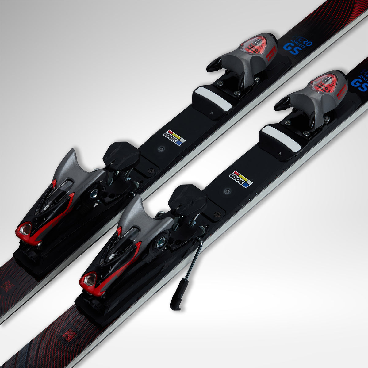Nahaufnahme von zwei Paar Rossignol HERO ATHLETE GS R22 2026/2027 Skiern mit Bindungen, schwarzen und roten Akzenten, nebeneinander auf einem hellgrauen Hintergrund.