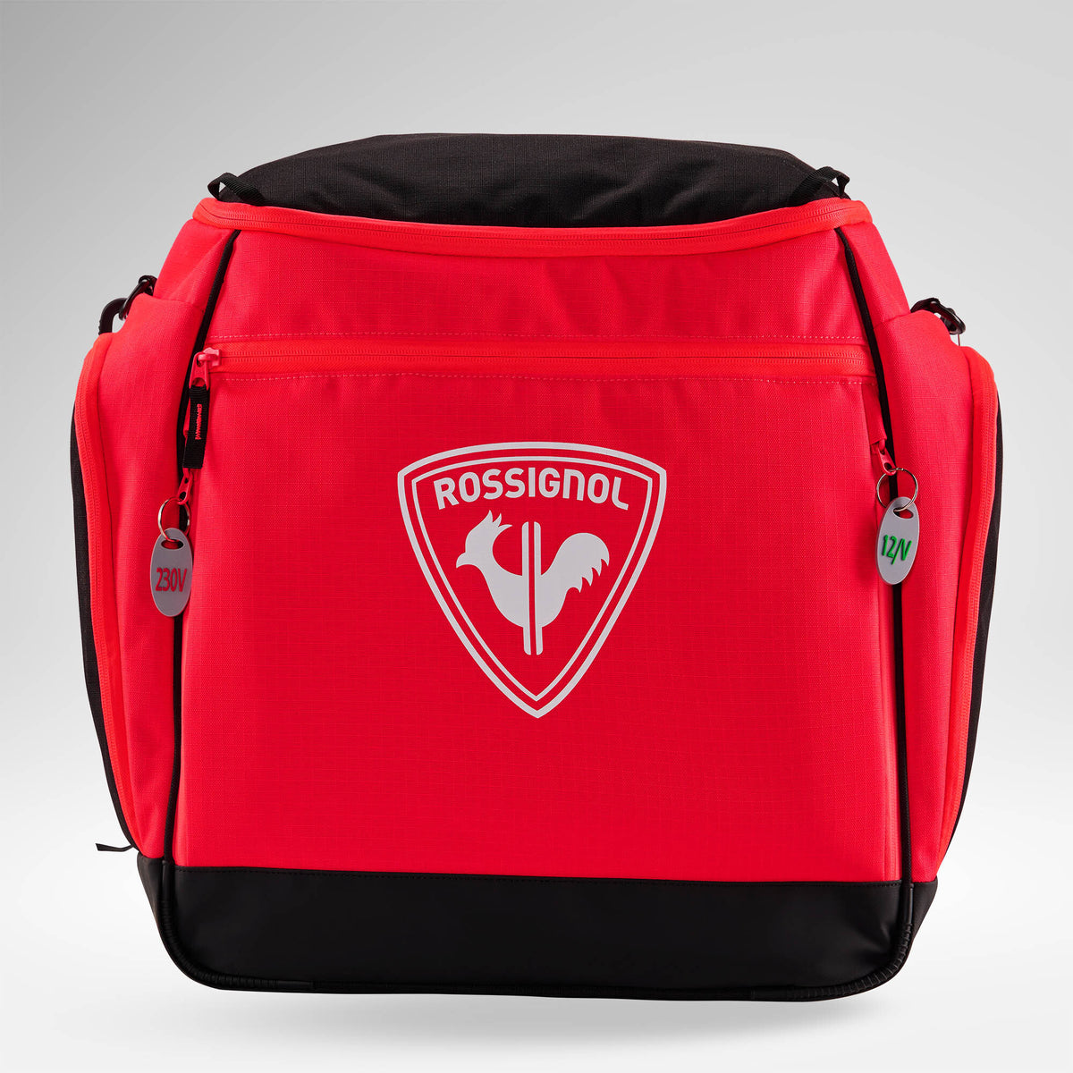 Eine leuchtend rote Rossignol HERO HEATED BAG 230V mit dem ikonischen weißen Hahn-Logo, einem robusten schwarzen Boden, praktischen Seitentaschen sowie zwei Reißverschlusslaschen mit den Aufschriften „230V“ und „12V“, sticht vor einem hellen Hintergrund mit Farbverlauf hervor – ideal für den Ski-Weltcup oder zum Warmhalten Ihrer Skiausrüstung dank integrierter Schuhheizung.