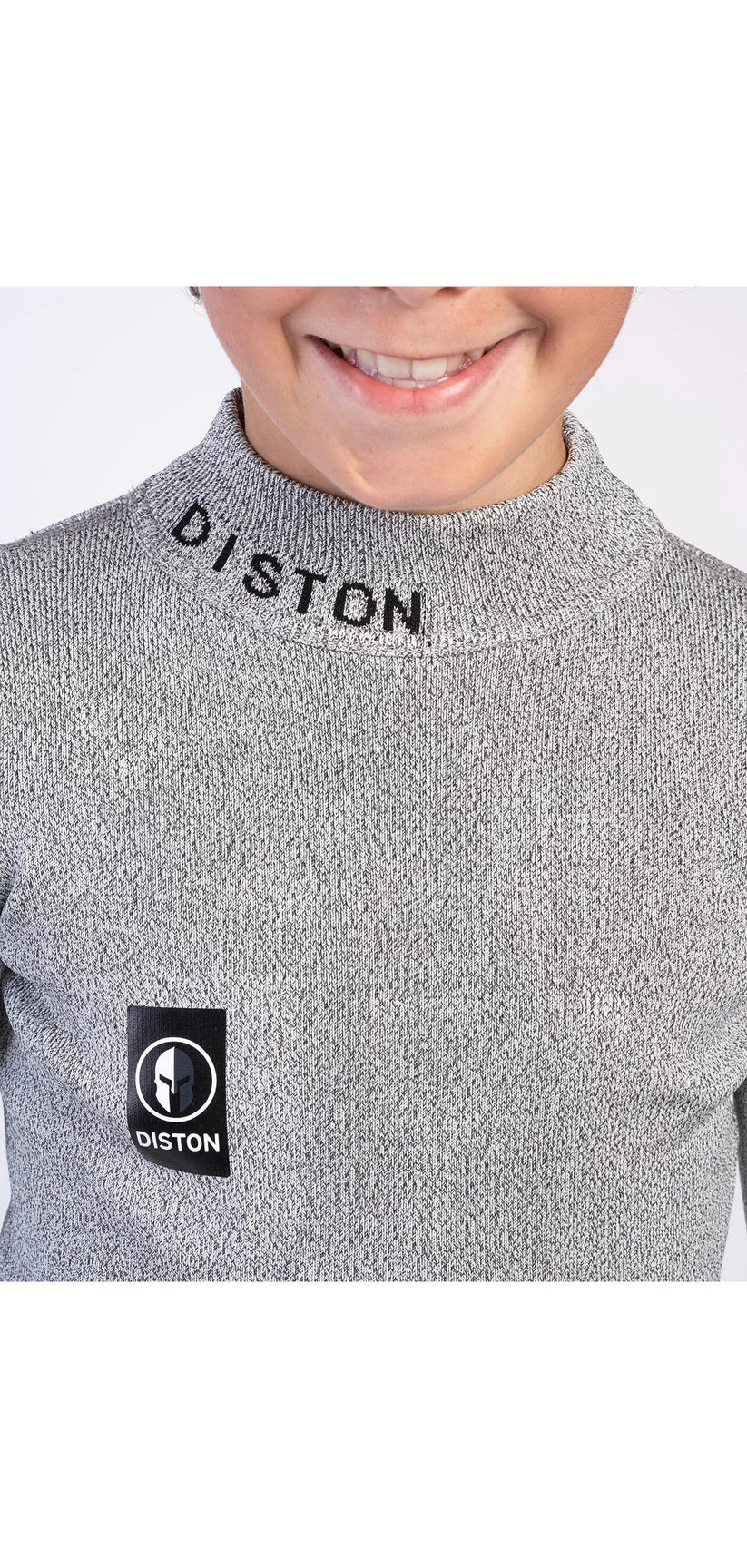 Ein Kind, möglicherweise ein Skirennfahrer, trägt das Diston Cut Resistant Top Junior - 3FIS Stars in CRG - BASE / Performance Fit mit "DISTON" auf dem Kragen und einem schwarz-weißen Diston-Brustlogo und lächelt, wobei sein Gesicht von der Nase abwärts sichtbar ist.