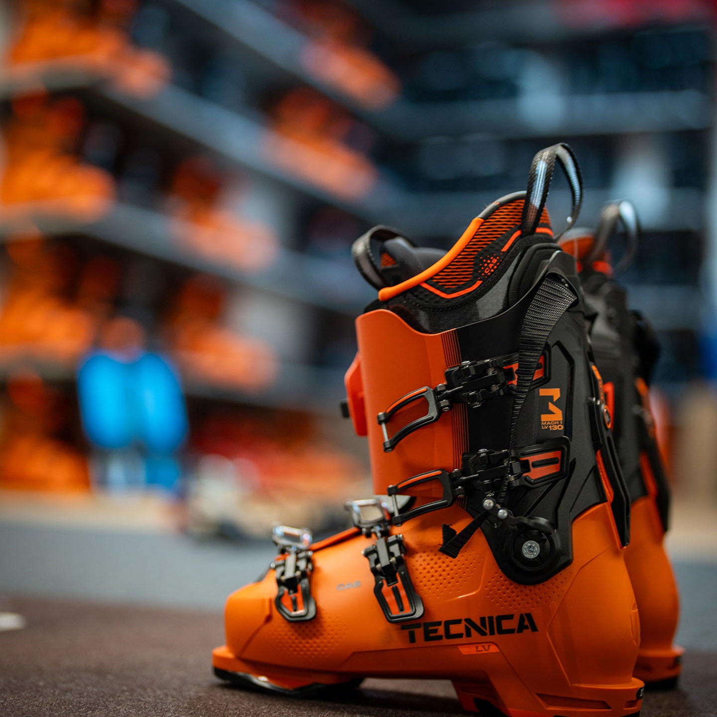 Tecnica Skischuhe Mach 1 LV 130 in leuchtendem Orange auf Ausstellungsflaeche im Sportfachgeschaeft – hochwertige Skischuhe fuer anspruchsvolle Skifahrer mit optimaler Passform und Performance.