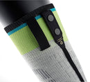 Eine Nahaufnahme von grauen und grünen SIDAS Ski race S.E.T Socken von Sidas mit einem schwarzen Riemen und zwei runden Knöpfen auf einem elektronischen Gerät mit der Aufschrift Power Button, das auf einem schwarzen Bein einer Schaufensterpuppe abgebildet ist.