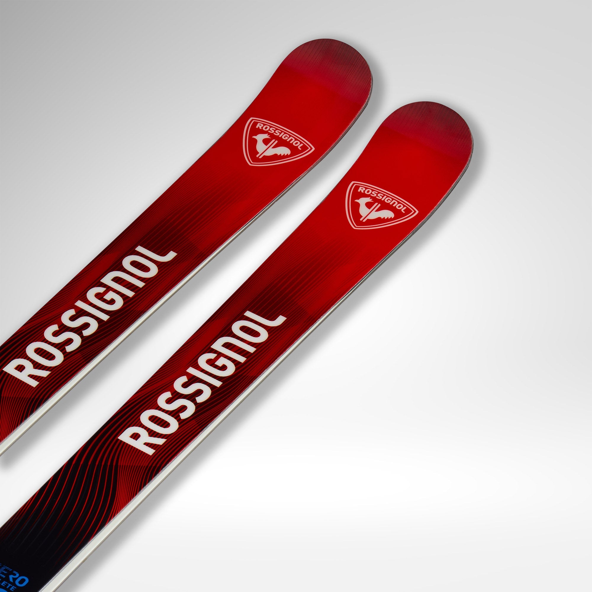 Zwei rote Rossignol-Skier mit weißen Logos und Text, dargestellt vor einem hellgrauen Hintergrund. Die Skispitzen sind sichtbar und tragen den Markennamen und das Emblem von Rossignol.