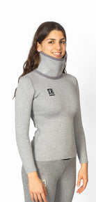 Eine Frau trägt das Diston DISTON WC Cut Resistant Top Women - 4FIS Stars in CRG - CORE / Racing Fit, ein graues, langärmeliges, hochgeschlossenes Oberteil mit einem Logo auf der Brust - ideal für Skirennläuferinnen, die Stil und Schutz suchen.