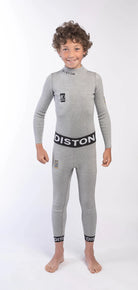 Ein lächelnder Junge mit lockigem Haar modelliert die DISTON Cut Resistant Underpants Junior - 4FIS Stars in CRG, CORE / Racing Fit von Diston. Er steht barfuß in einem hellgrauen Ganzkörper-Neoprenanzug vor einem schlichten weißen Hintergrund.