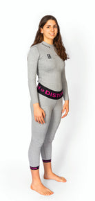 Eine Frau mit langen braunen Haaren steht barfuß, lächelt und trägt eine Diston WC Cut Resistant Unterhose für Frauen-4FIS Stars in CRG, CORE / Racing Fit-mit "DISTON" auf dem Bund, vor einem weißen Hintergrund.