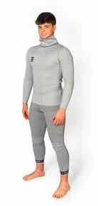 Ein junger Mann steht barfuß, lächelnd, in einem taillierten Diston DISTON WC Cut Resistant Top Men - 4FIS Stars in CRG - CORE / Racing Fit. Das hellgraue Outfit wirkt weich und warm - perfekt für Skirennläufer. Der Hintergrund ist einfarbig weiß.