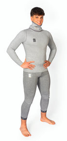 Eine lächelnde Person steht barfuß mit den Händen in den Hüften und trägt ein passendes graues Diston DISTON WC Cut Resistant Top Men - 4FIS Stars in CRG - CORE / Racing Fit und eine für Wasseraktivitäten konzipierte Hose vor einem weißen Hintergrund.