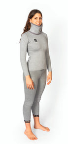 Eine barfüßige Frau lächelt, sie trägt das Diston DISTON WC Cut Resistant Top Women - 4FIS Stars in CRG - CORE / Racing Fit und die dazu passende Hose mit Logodetails - ideale schnittfeste Unterwäsche für Skirennläuferinnen - vor einem weißen Hintergrund.