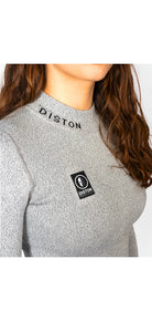 Eine Frau mit langen braunen Haaren trägt das Diston WC Cut Resistant Top Women - 4FIS Stars in CRG - CORE / Racing Fit mit grauem Rippenmuster, gesticktem "DISTON" in der Nähe des Kragens und einem schwarz-weißen rechteckigen Logoaufnäher auf der Brust.