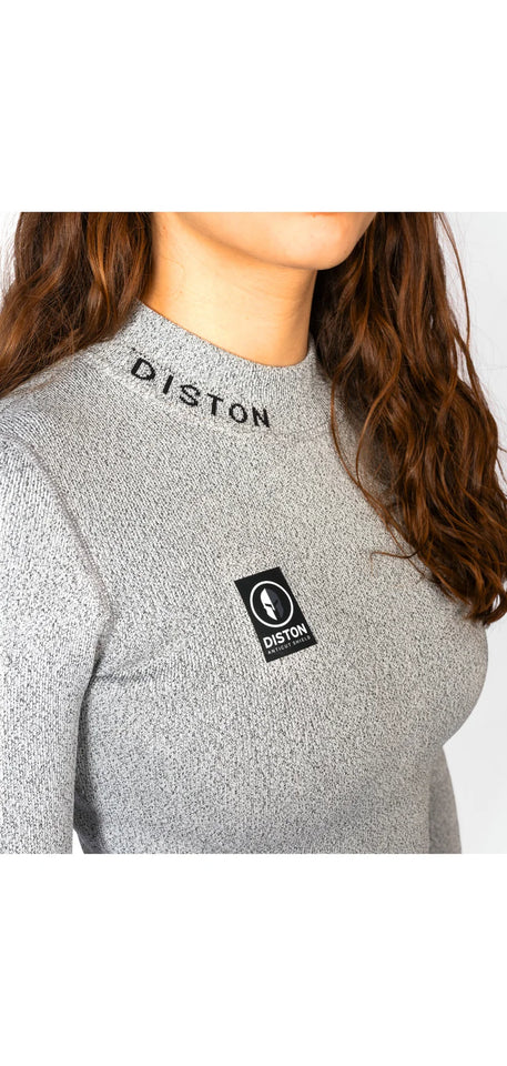 Eine Frau mit langen braunen Haaren trägt das Diston WC Cut Resistant Top Women - 4FIS Stars in CRG - CORE / Racing Fit mit grauem Rippenmuster, gesticktem "DISTON" in der Nähe des Kragens und einem schwarz-weißen rechteckigen Logoaufnäher auf der Brust.
