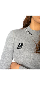 Eine Frau verschränkt die Arme, während sie das Diston WC Cut Resistant Top Women (CORE/Racing Fit, 4FIS Stars in CRG), in Hellgrau mit "DISTON" am Kragen und schwarzem Logoaufnäher, modelliert - ideal für sicherheits- und stilbewusste Skirennläuferinnen.