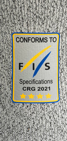 Ein rechteckiger Aufnäher auf grauem Strick für das Diston DISTON WC Cut Resistant Top Women - 4FIS Stars in CRG - CORE / Racing Fit zeigt "CONFORMS TO FIS Specifications CRG 2021", mit einem blauen und gelben Swoosh über fünf gelben Sternen.