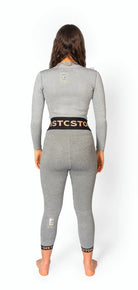 Eine Frau mit langen braunen Haaren steht barfuß, den Blick abgewandt, und trägt eine graue Diston DISTON WC Cut Resistant Unterhose für Frauen mit schwarzen und orangefarbenen Streifen und kleinen Logoaufnähern auf dem Rücken.