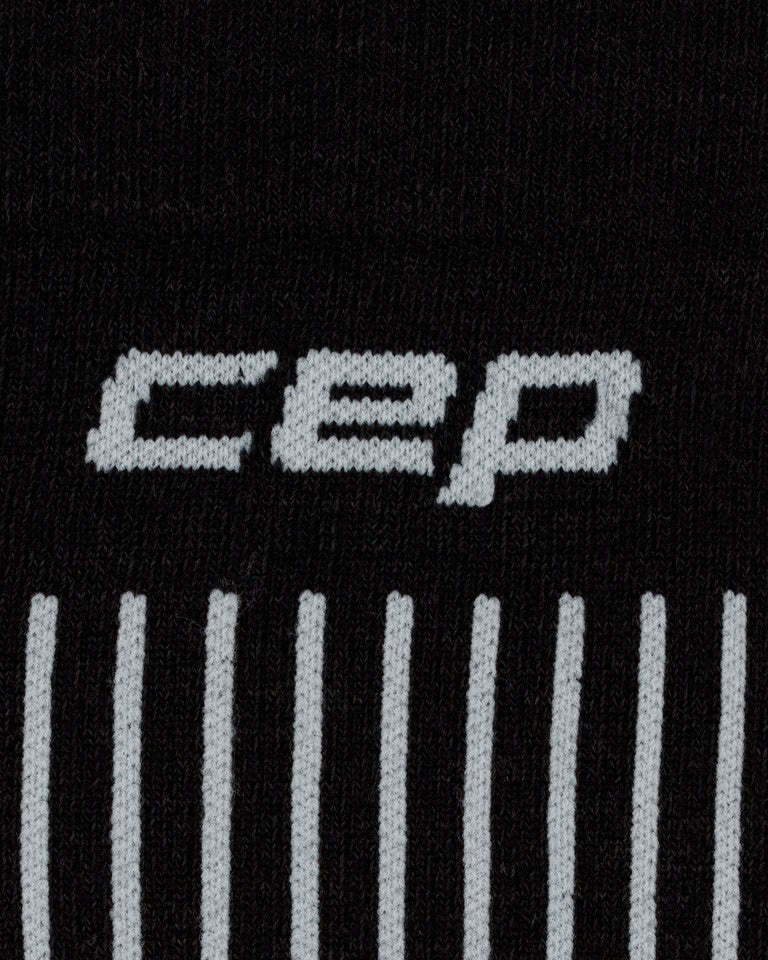 Die CEP Ski Ultralight Socken 3.0 in Schwarz/Grau für Damen bestehen aus schwarzem Stoff, auf dem im oberen Bereich der Schriftzug „CEP“ in Weiß eingestrickt ist; darunter befinden sich mehrere vertikale weiße Linien, die das charakteristische Design der Marke unterstreichen.