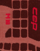Nahaufnahme der CEP Ski Ultralight Socken 3.0 in Braun und Dunkelrot für Herren, die ein gestricktes geometrisches Muster mit gitterartigen Quadraten und rot aufgestickten Symbolen auf der rechten Seite zeigen.