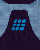 Nahaufnahme der CEP Ski Ultralight Socken 3.0 (dunkelviolett/blau, Damen) von CEP, mit einem Strickmuster im geometrischen Design – ein zentraler dunkelvioletter Bereich, der in der Mitte durch hellblaue und türkisfarbene Formen akzentuiert wird und von hellblauen Bereichen umgeben ist.