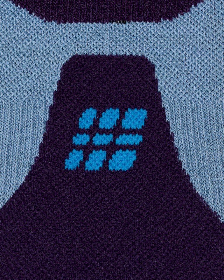 Nahaufnahme der CEP Ski Ultralight Socken 3.0 (dunkelviolett/blau, Damen) von CEP, mit einem Strickmuster im geometrischen Design – ein zentraler dunkelvioletter Bereich, der in der Mitte durch hellblaue und türkisfarbene Formen akzentuiert wird und von hellblauen Bereichen umgeben ist.
