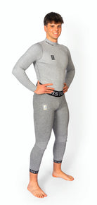 Eine lächelnde Person steht barfuß vor einem weißen Hintergrund und trägt eine Diston DISTON WC Cut Resistant Unterhose Men - 5FIS Stars in CRG - PRO/Racing Compression Fit, hellgrau mit schwarzem Bund und Knöchelbesatz.