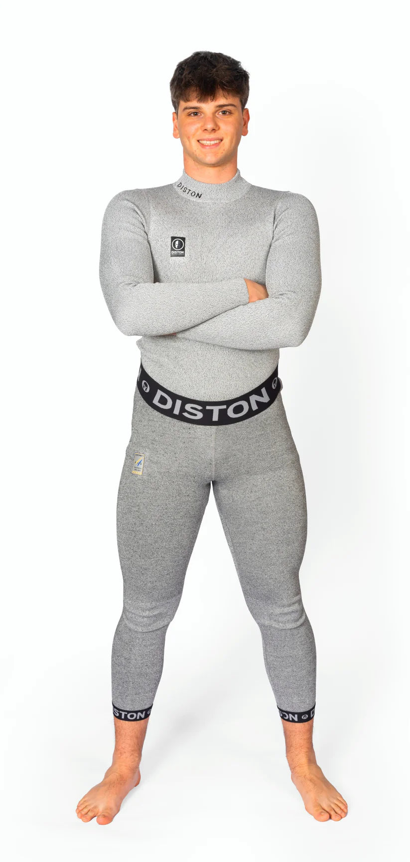 Ein junger Mann steht barfuß, lächelnd und mit verschränkten Armen in einer Diston WC Cut Resistant Unterhose Men - 5FIS Stars in CRG - PRO/Racing Compression Fit vor einem schlichten weißen Hintergrund.