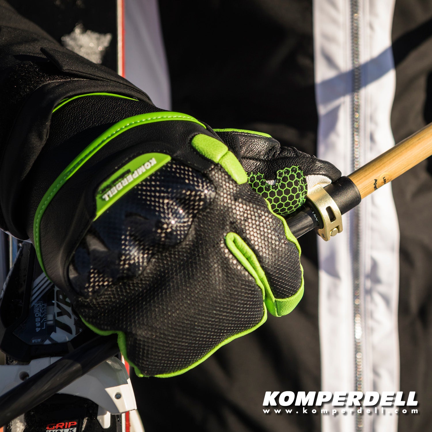 Detailansicht des Komperdell Racing Lobster Handschuhs fuer Erwachsene in schwarz-gruen mit Protektor und rutschfester Handflaeche beim Greifen eines Skistocks