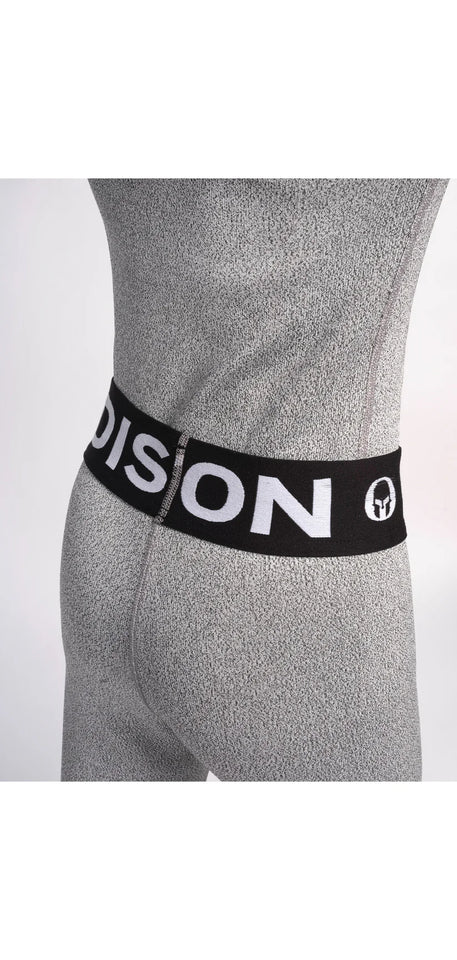 Nahaufnahme einer Person, die Diston Cut Resistant Underpants Junior trägt - hellgraue, strukturierte Sportleggings mit schwarzem Bund und auffälligem weißem "DISTON"-Schriftzug und Logo. Ideal für Skirennläufer. Einfarbig weißer Hintergrund.