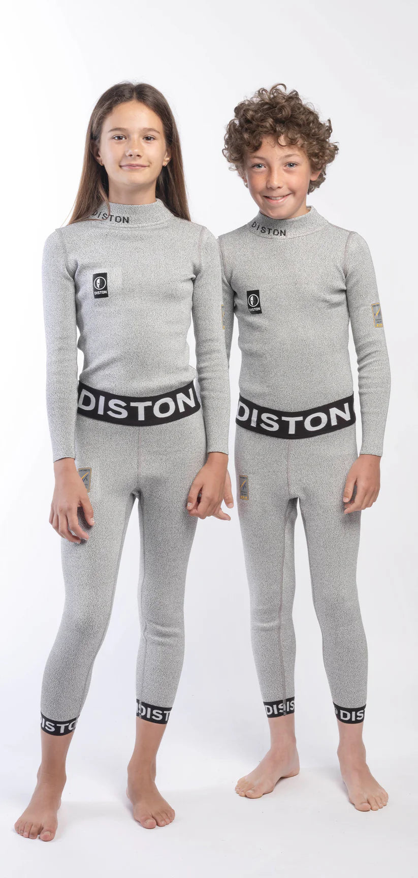 Zwei Kinder stehen nebeneinander in passenden hellgrauen Diston Cut Resistant Unterhosen Junior - 3FIS Stars in CRG (BASE / Performance Fit) mit schwarzem und weißem Diston-Branding am Bund und an den Bündchen vor einem schlichten weißen Hintergrund.