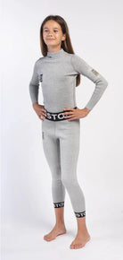 Ein junges Mädchen steht barfuß auf einem weißen Hintergrund, lächelt und blickt zur Seite. Es trägt eine Diston DISTON Cut Resistant Unterhose Junior - 3FIS Stars in CRG - BASE / Performance Fit mit schwarzen und weißen Markenbündchen.