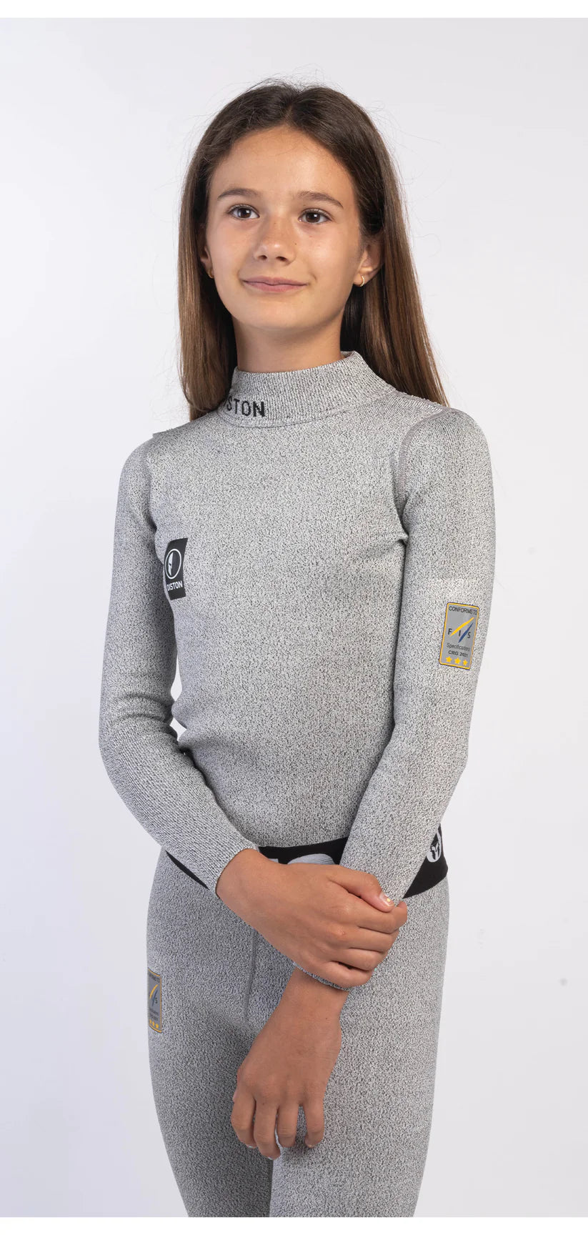 Ein junges Mädchen mit langen braunen Haaren trägt eine Diston DISTON Cut Resistant Unterhose Junior - 3FIS Stars in CRG, Performance Fit BASE, steht vor einem schlichten weißen Hintergrund und lächelt leicht zur Seite.
