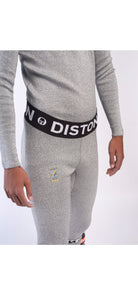 Eine Person trägt DISTON WC Schnittfeste Hosen Herren - 4FIS Stars in CRG - CORE / Racing Fit by Diston: hellgraues, langärmeliges Thermo-Oberteil und Leggings mit schwarzem DISTON-Bund. Nur Torso und Oberschenkel sind auf weißem Grund sichtbar.