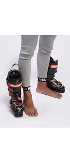 Eine Person, die eine Diston DISTON WC Schnittfeste Hosen Herren - 4FIS Stars in CRG - CORE / Racing Fit schnittfeste Hose trägt, zieht schwarze und rote Skischuhe an, wobei ein Fuß in einem Schuh steckt und der andere neben einem offenen Schuh steht.