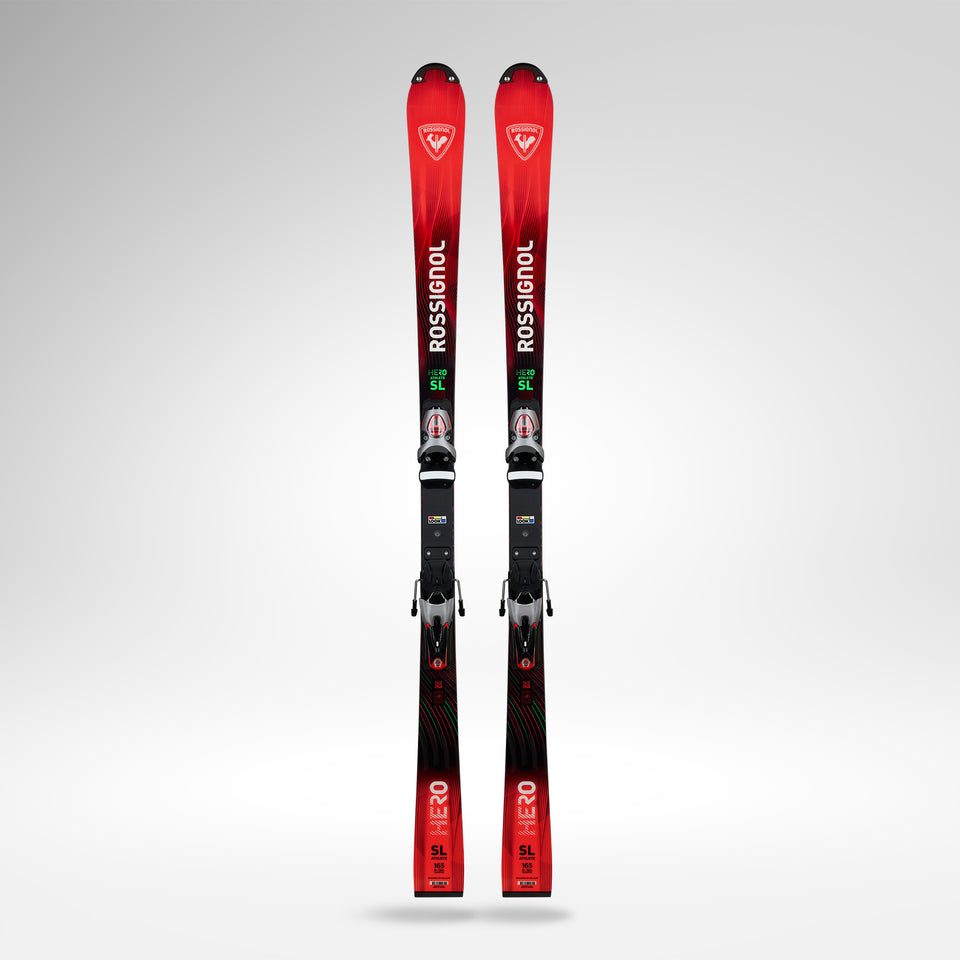 Ein Paar rote und schwarze Rossignol HERO FIS SL 157 R22 2026/2027 Skier mit Bindungen stehen aufrecht vor einem schlichten hellgrauen Hintergrund.