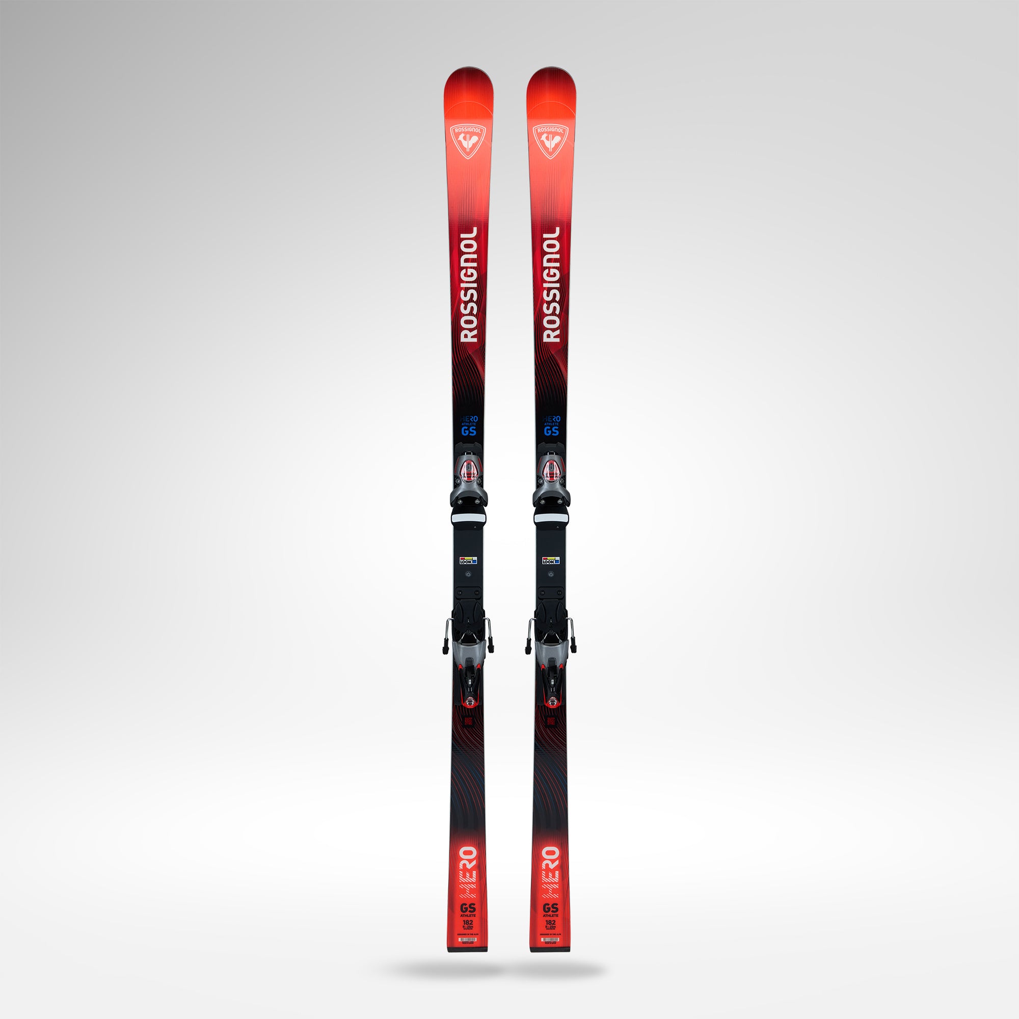 Ein Paar Rossignol HERO ATHLETE GS R22 2026/2027 Skier mit Bindungen in Rot und Schwarz stehen aufrecht vor einem hellgrauen Hintergrund - perfekt für ambitionierte U14- und U16-Rennfahrer.
