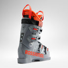 Der Rossignol HERO WORLD CUP 90 SC - POWER GREY 2026/2027 Junioren-Skischuh ist in Grau und Orange gehalten, hat schwarze Schnallen und Riemen und zeigt das Rossignol-Logo in Orange an der Seite auf weißem Grund.