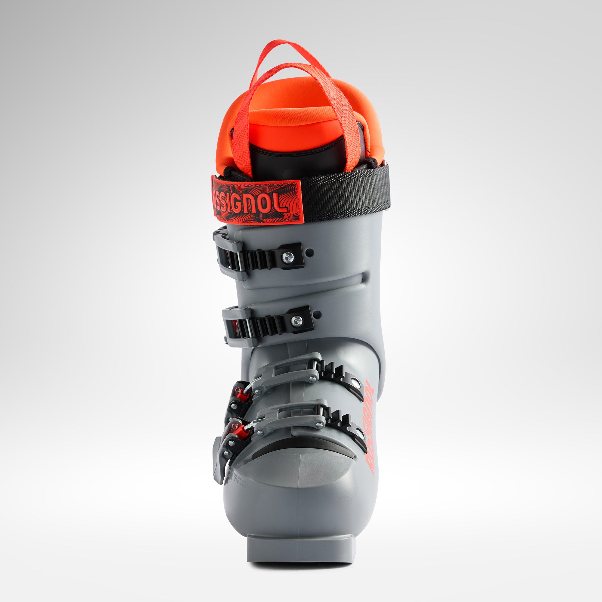Ein einzelner Rossignol HERO WORLD CUP 70 SC - POWER GREY 2026/2027 Junior-Skischuh mit roten Akzenten, schwarzen Schnallen und orangefarbenem Innenfutter steht aufrecht auf einem schlichten hellen Hintergrund.