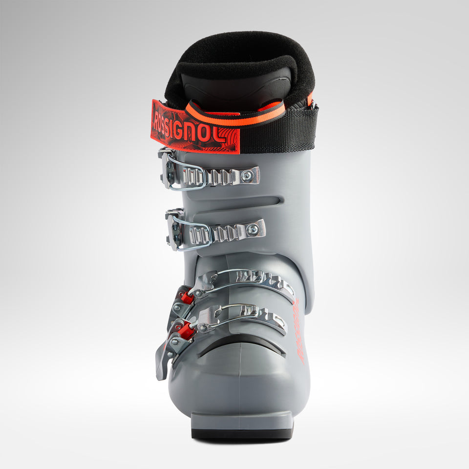 Ein Rossignol HERO JR 65 - POWER GREY 2026/2027 Junior-Skischuh mit vier Metallschnallen und einem schwarz-roten Oberriemen ist von vorne vor einem schlichten, hellen Hintergrund abgebildet.