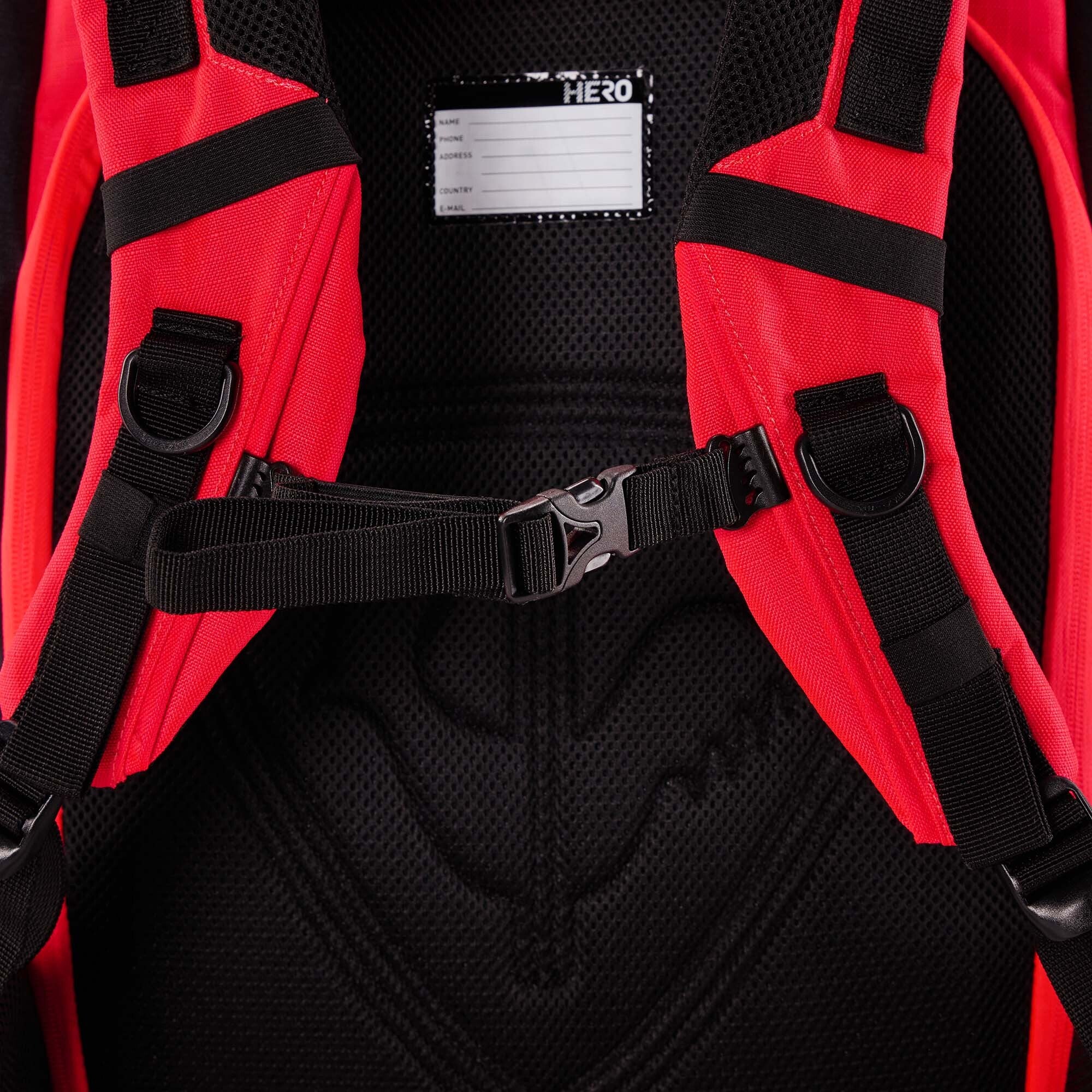 Nahaufnahme der roten Schultergurte, der Brustschnalle und der Netzpolsterung des Rossignol HERO ATHLETES BAG. Oben ist ein kleines Etikett zum Beschriften mit dem Namen zu sehen, das das praktische Design dieses wasserdichten Rossignol-Rucksacks unterstreicht.