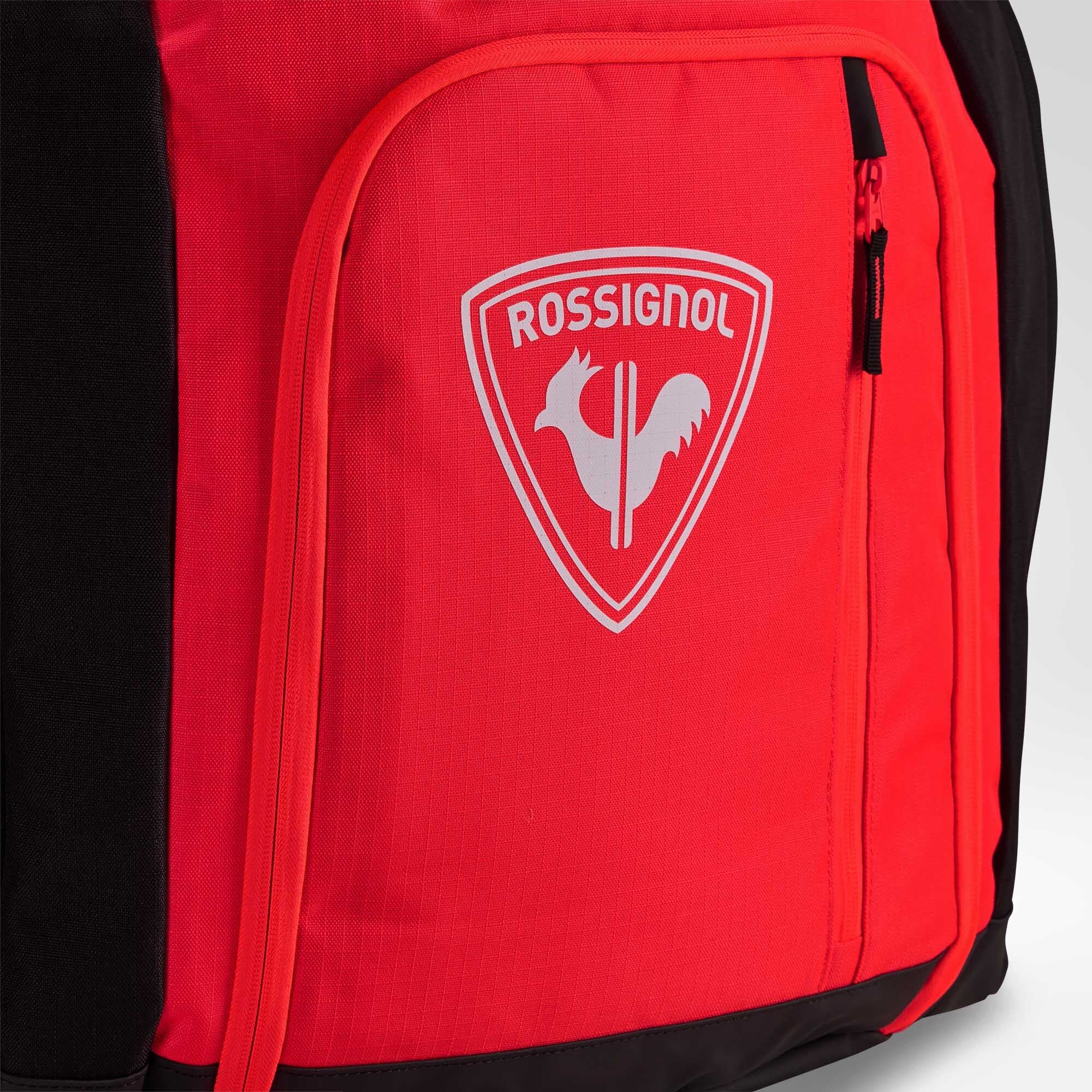Nahaufnahme einer roten Rossignol HERO ATHLETES BAG mit einer Reißverschlusstasche, auf deren Vorderseite das weiße Rossignol-Logo und das Hahn-Emblem zu sehen sind.