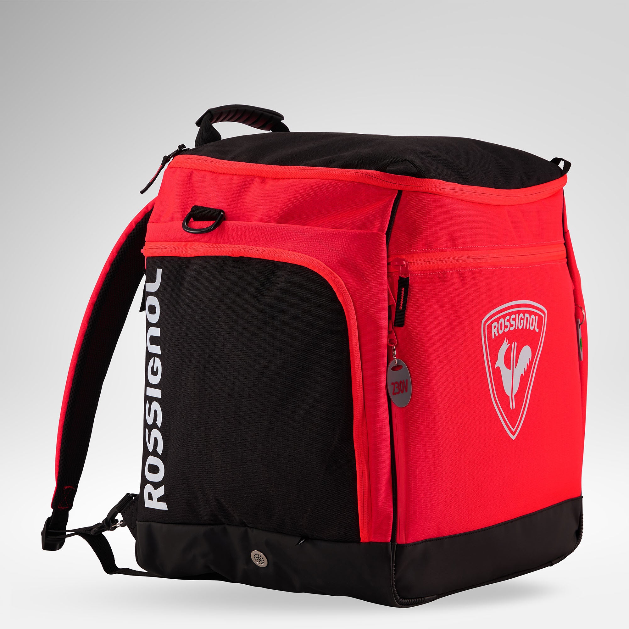 Eine rot-schwarze Rossignol HERO HEATED BAG 230V mit Reißverschlusstaschen an den Seiten und vorne, gepolsterten Schultergurten und einem großen Logo auf grauem Hintergrund – perfekt kombinierbar mit Ihrer Skischuhtasche oder beheizbaren Stiefeltasche für all Ihre Abenteuer in den Alpen.