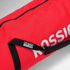Nahaufnahme einer roten Rossignol HERO SKI BAG 2/3P ADJUSTABLE 190/220 mit einem schwarzen Griff und einem Etikett mit der Aufschrift „2/3 PAIRS 190/220CM“. Die Tasche verfügt über einen Reißverschluss, ein Teil des Rossignol-Logos ist zu sehen, und dank ihrer verstellbaren Länge eignet sie sich ideal als Skitasche 220 cm für die flexible Aufbewahrung von Skiern.