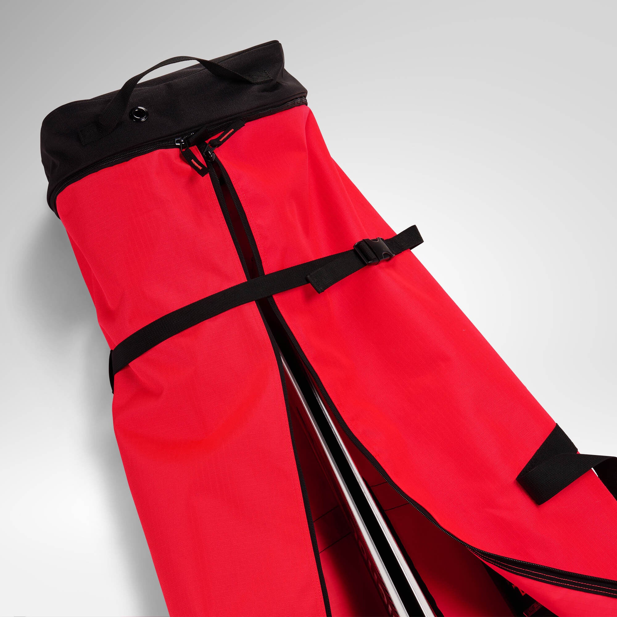 Eine rot-schwarze Rossignol HERO SKI BAG 2/3P ADJUSTABLE 190/220 mit schwarzen Riemen und Reißverschlüssen ist teilweise geöffnet abgebildet, sodass die darin befindliche Sportausrüstung auf einer hellgrauen Unterlage zu sehen ist – was das robuste Design unterstreicht, das an die renommierte Marke Rossignol erinnert.