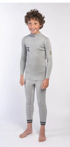 Ein Junge mit lockigem Haar steht barfuß, lächelnd und trägt ein passendes hellgraues Diston DISTON Cut Resistant Top Junior - 4FIS Stars in CRG - CORE / Racing Fit Set mit schwarzer Beschriftung vor einem schlichten weißen Hintergrund.