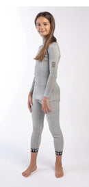 Ein junges Mädchen mit langen braunen Haaren steht barfuß vor einem weißen Hintergrund, trägt das Diston DISTON Cut Resistant Top Junior - 4FIS Stars in CRG - CORE / Racing Fit und passende Leggings mit schwarzen Bündchen, posiert und lächelt leicht in die Kamera.